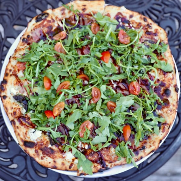 Dieci Pizza's pizza with arugula, cherry tomatoes, and balsamic glaze on a white plate.