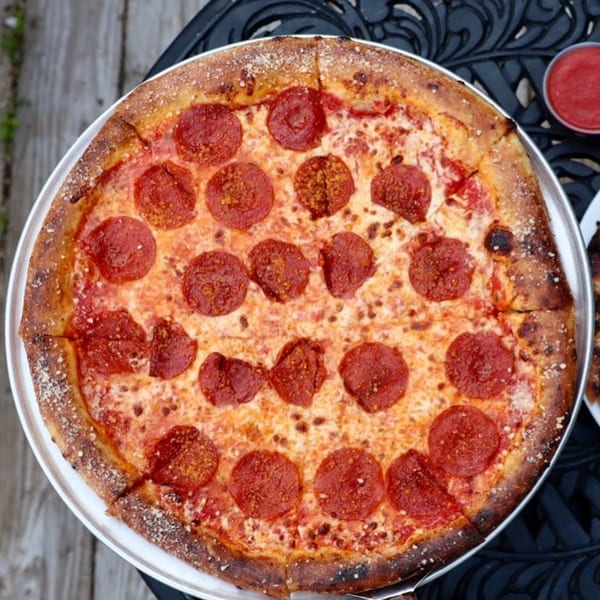 A whole pepperoni pizza from Dieci Pizza Pensacola, with a side of red sauce.